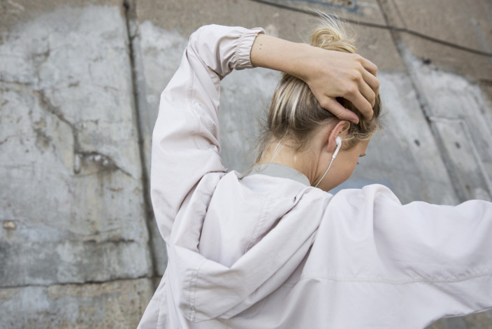 Junge Frau mit In-Ear-Kopfhörern fasst sich an den Hinterkopf