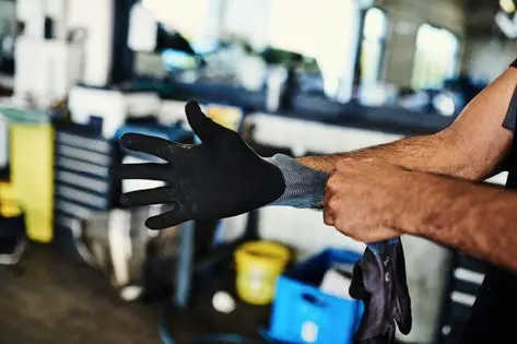Mann in einer Werkstatt zieht sich Arbeitshandschuhe an. 