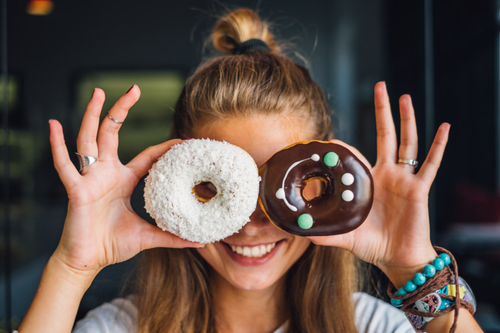 junge Frau schaut lachend durch zwei bunt dekorierte Donuts