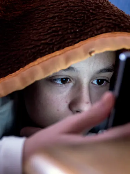 Kind schaut, versteckt unter eine Decke, auf das Display eines Smartphones