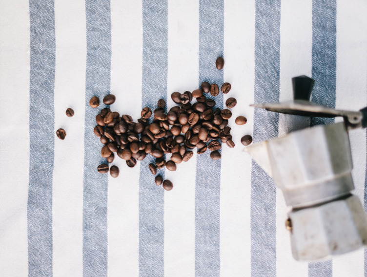 Espressokanne und Kaffeebohnen auf einer gestreiften Tischdecke.