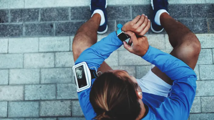 Ein in Sportsachen gekleideter, junger Mann, der auf seine Smartwatch guckt. 