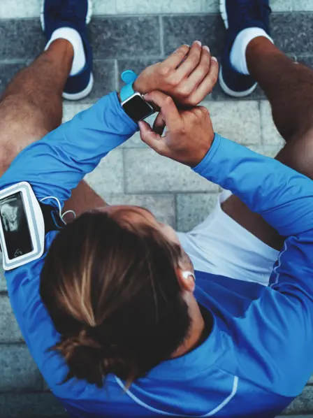 Ein in Sportsachen gekleideter, junger Mann, der auf seine Smartwatch guckt. 
