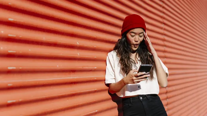 Junge Frau schaut erstaunt in ihr Smartphone.