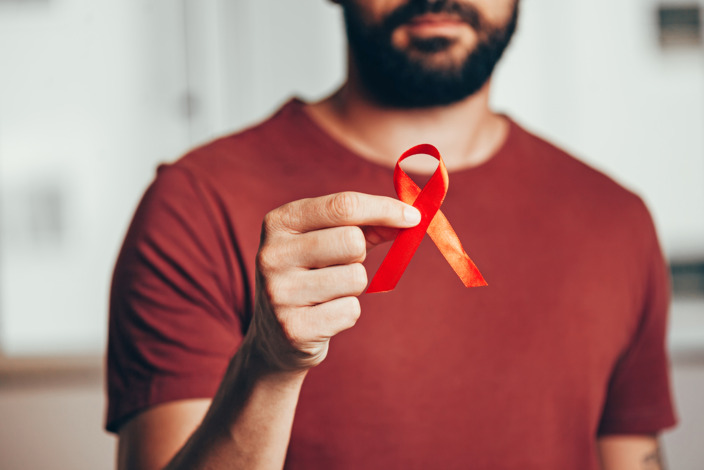 Mann hält eine rote Schleife zur Solidarisierung zum Welt-Aids-Tag in der Hand