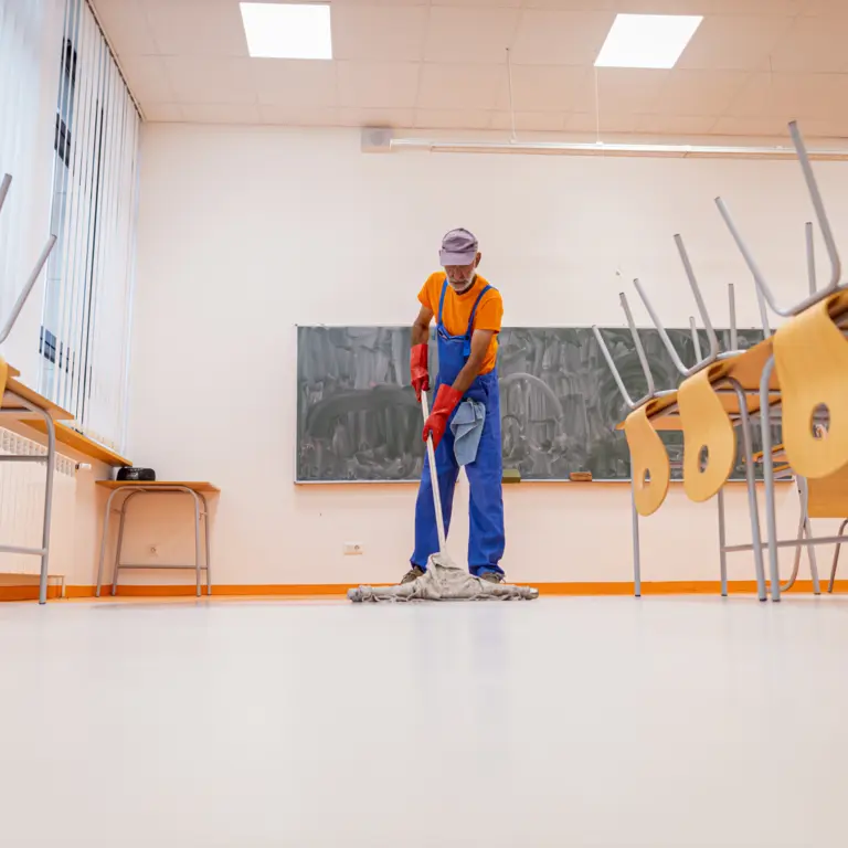 Reinigungskraft wischt Boden in Klassenzimmer.