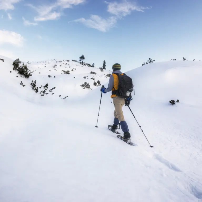 Mann auf Schneeschuhen wandert mit Skistöcken durch eine Schneelandschaft