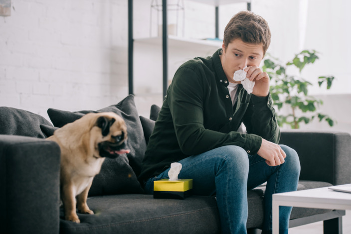 Mann sitzt mit Taschentuch neben Hund auf dem Sofa