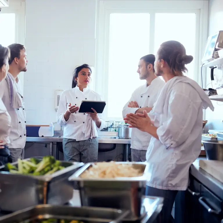 Köche und Köchinnen stehen gemeinsam in der Küche und besprechen sich