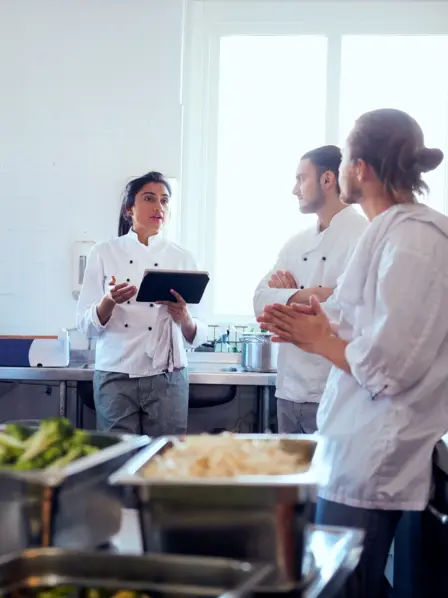 Köche und Köchinnen stehen gemeinsam in der Küche und besprechen sich