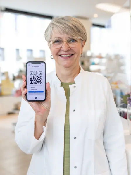 Neuerungen im Gesundheitswesen: Eine Pharmazeutin im weißen Kittel zeigt ein Handy, auf dem ein E-Rezept geöffnet ist.