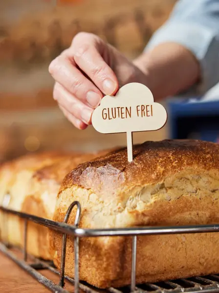 Jemand steckt ein mit glutenfrei beschriftetes Schild in ein Brot