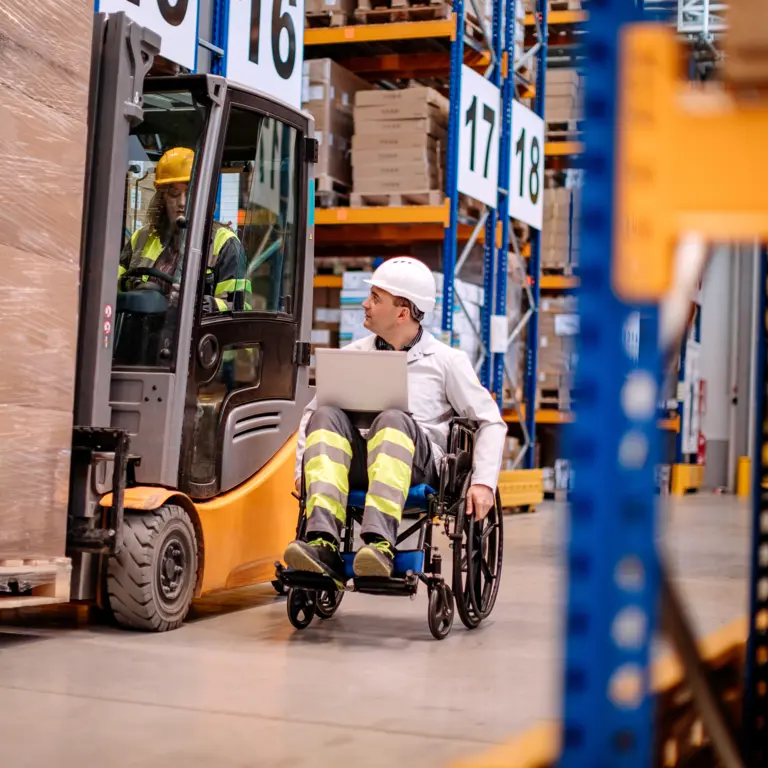 Ein Mann sitzt im Rollstuhl und fährt durch eine Fabrikhalle. 