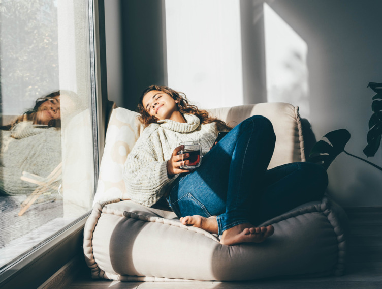 Frau liegt auf dem Sofa vor der Fensterscheibe im Sonnenlicht