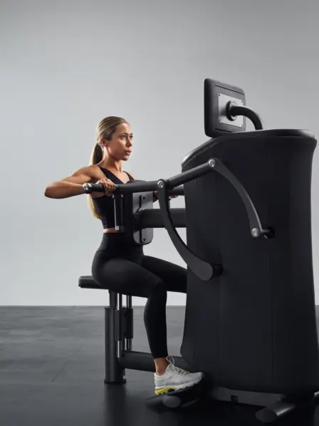 Frau sitzt an einem Fitnessgerät und trainiert