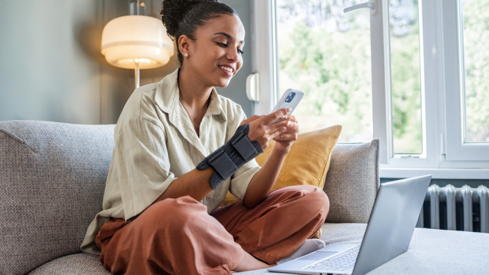 Junge Frau mit Handbandage sitzt vor ihrem Laptop