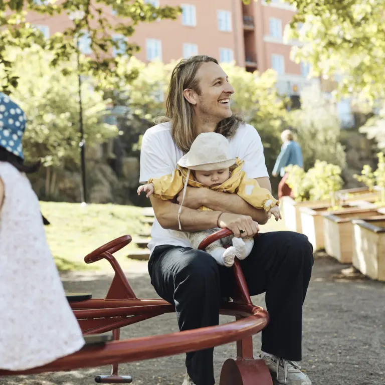 Familienvater mit einen zwei Kleinkindern auf einem Spielplatz.
