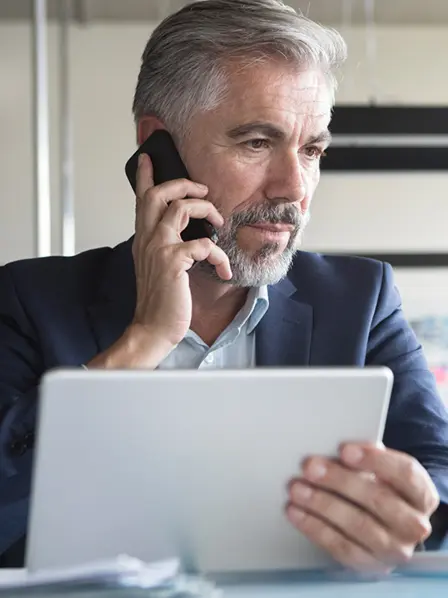 Mann sitzt vor zwei Bildschirmen und telefoniert am Handy