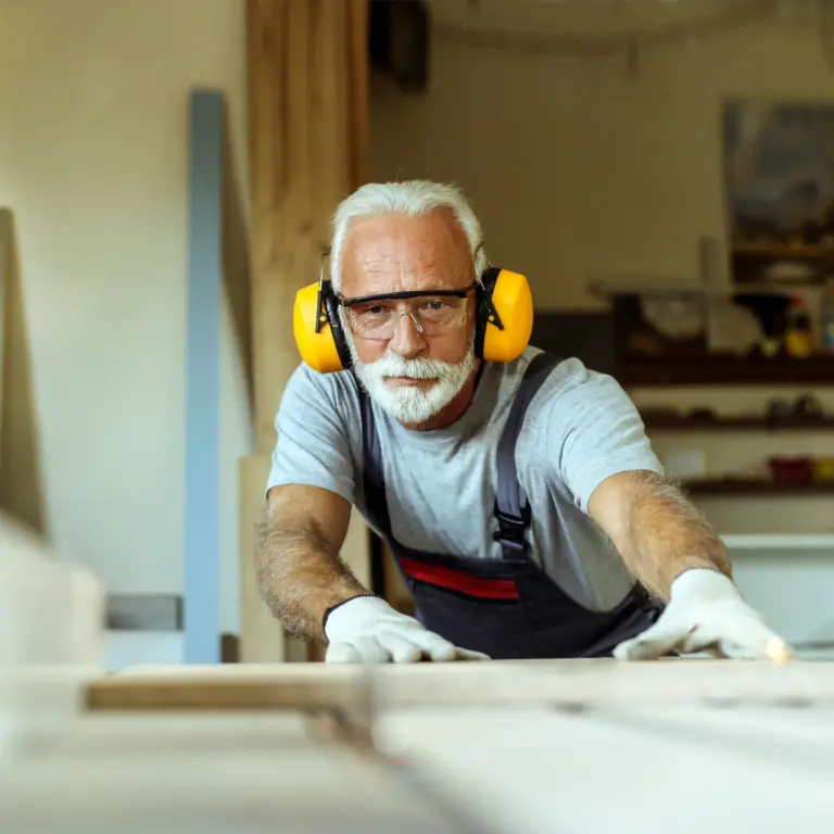 Ein älterer Mann schneidet Holz in einer Werkstatt. 