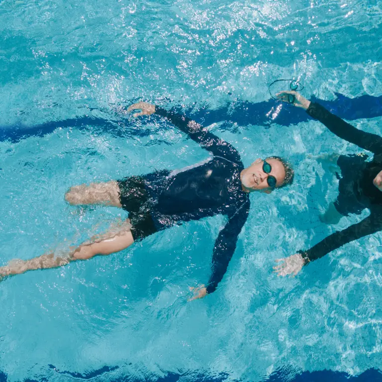 Ein Erwachsener nimmt Schwimmunterricht und lässt sich auf dem Rücken im Wasser treiben.