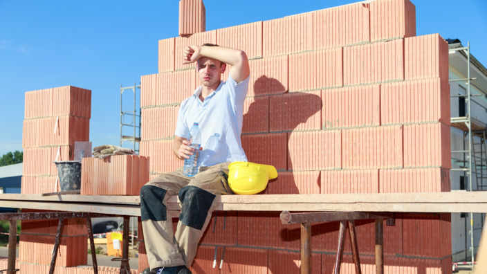 Person auf der Baustelle, sitzt in der Sonne und schwitzt.