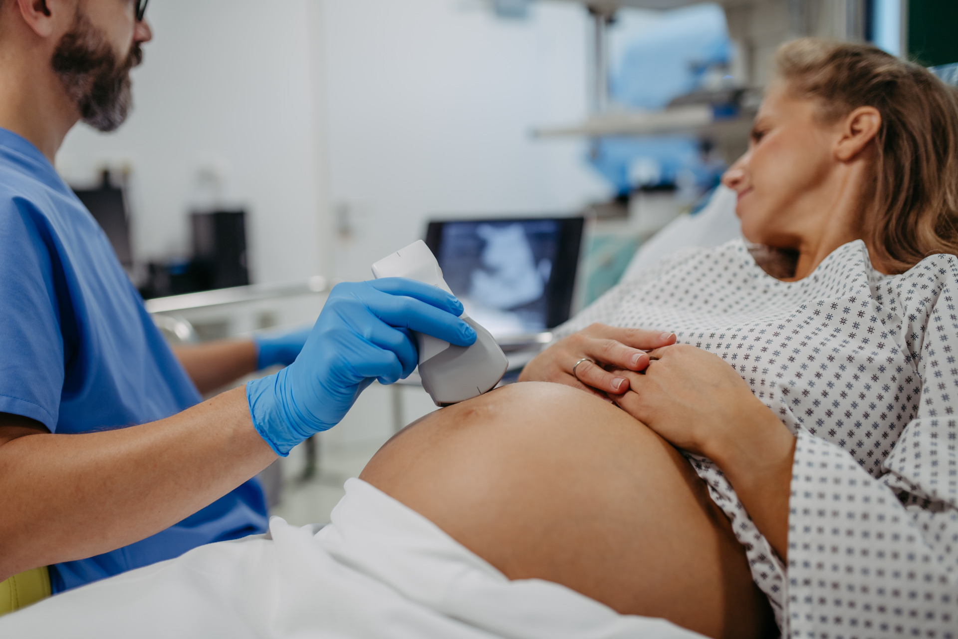 Eine schwangere Frau liegt entspannt, ein Arzt führt mit einem Ultraschallgerät eine Untersuchung ihres Bauches in einer Klinik durch.