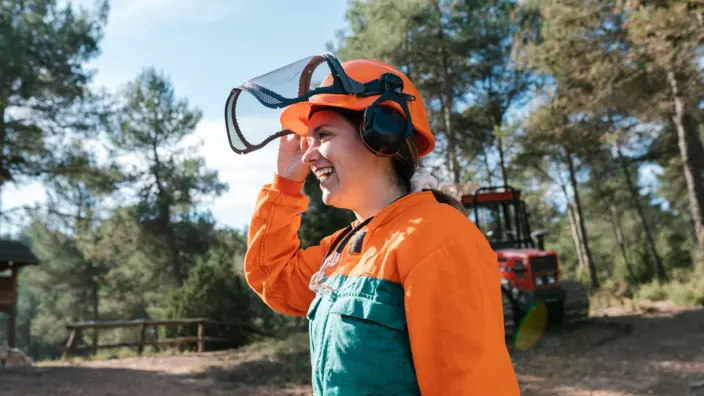 Frau in Arbeitsoverall beim Bäumefällen im Wald.
