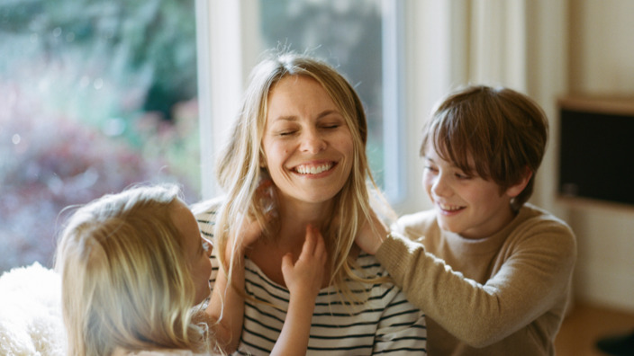 Junge Mutter sitzt lachend mit Kindern auf dem Sofa