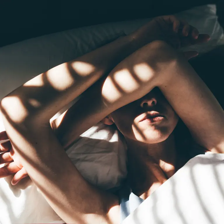 Frau im Bett, die sich die Arme schützend vor das Gesicht hält