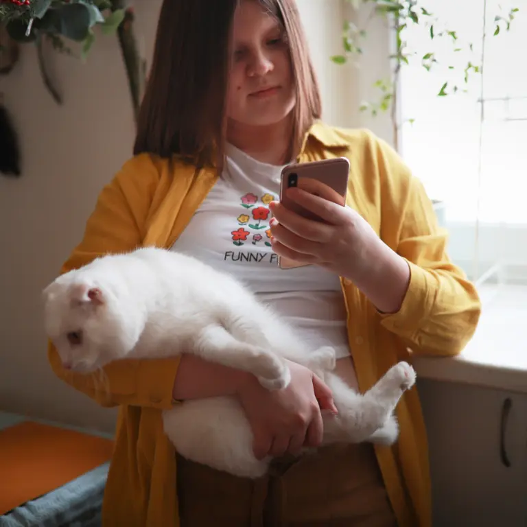 Ein übergewichtiges Kind hält eine Katze auf dem Arm und schaut auf ein Smartphone – Symbolbild für Übergewicht bei Kindern