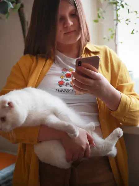Ein übergewichtiges Kind hält eine Katze auf dem Arm und schaut auf ein Smartphone – Symbolbild für Übergewicht bei Kindern