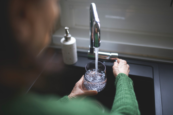 Frau lässt Leitungswasser in ihr Glas am Spülbecken laufen