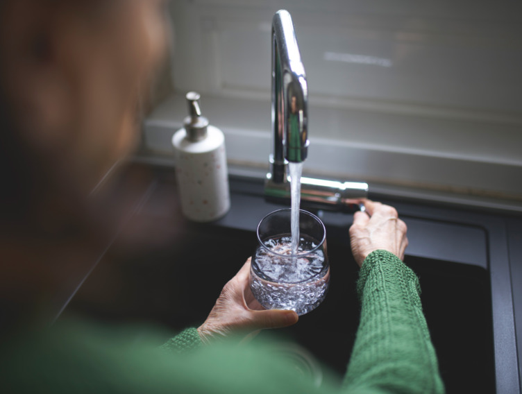 Frau lässt Leitungswasser in ihr Glas am Spülbecken laufen