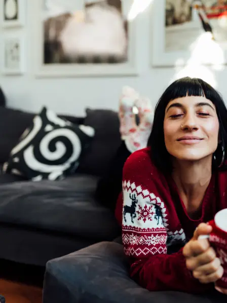 Frau liegt mit geschlossenen Augen auf einem Sofa mit einer Tasse in der Hand