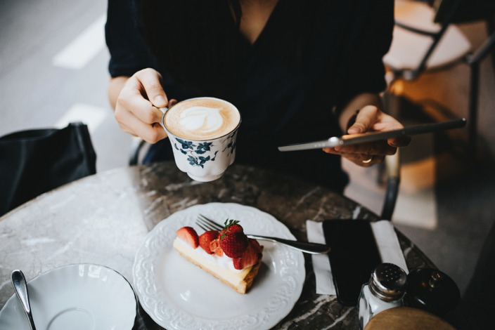 Frau sitzt an einem Tisch mit einer Tasse Kaffee und einem Stück Erdbeerkuchen.