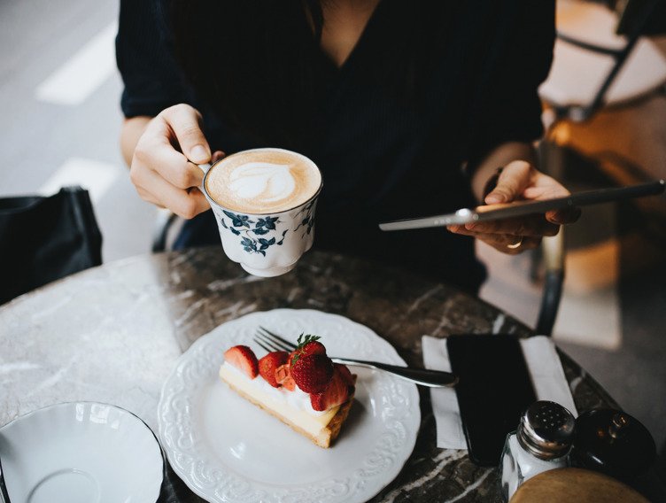 Frau sitzt an einem Tisch mit einer Tasse Kaffee und einem Stück Erdbeerkuchen.