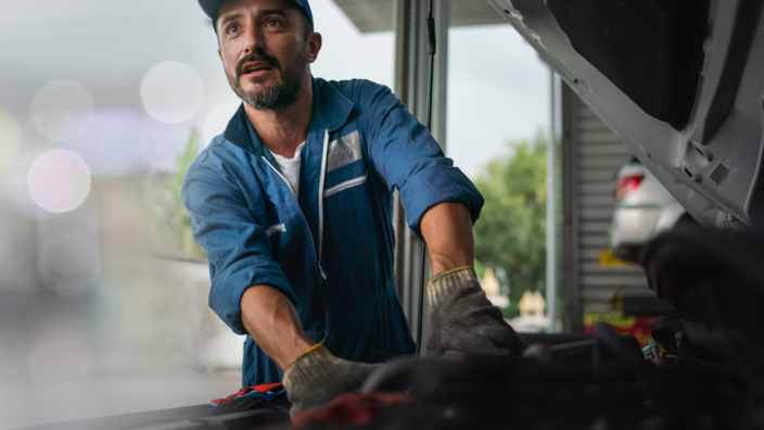 Handwerker steht in der Werkstatt an einem Auto mit geöffneter Motorenklappe