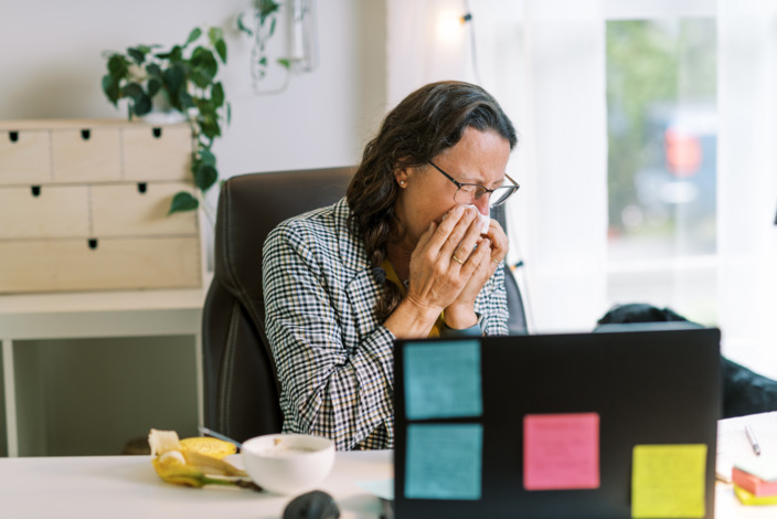 Büroangestellte sitzt schnäuzend an ihrem Schreibtisch