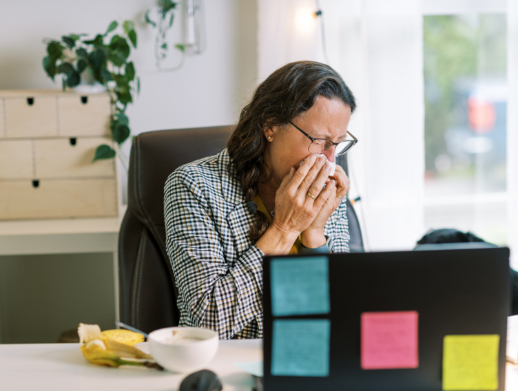 Büroangestellte sitzt schnäuzend an ihrem Schreibtisch