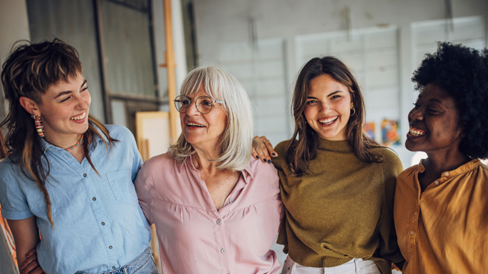 4 Frauen nebeneinander, lächelnd. 