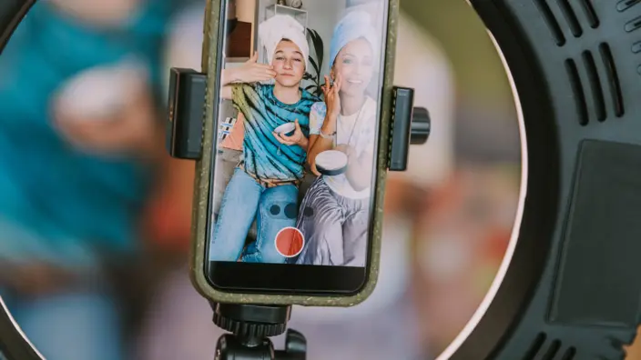 Auf einem Handyscreen sieht man zwei junge Frauen, wie sie sich lächelnd das Gesicht eincremen.