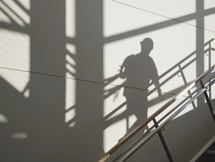 Treppenhaus mit Geländer, in dem man einen Beschäftigten als Schatten an der Wand sieht.