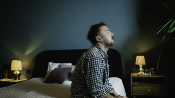 Mann sitzt in einem dunklen Schlafzimmer auf der Bettkante.