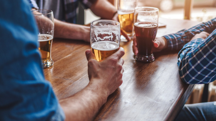 Männer sitzen an einem Holztisch und trinken Bier