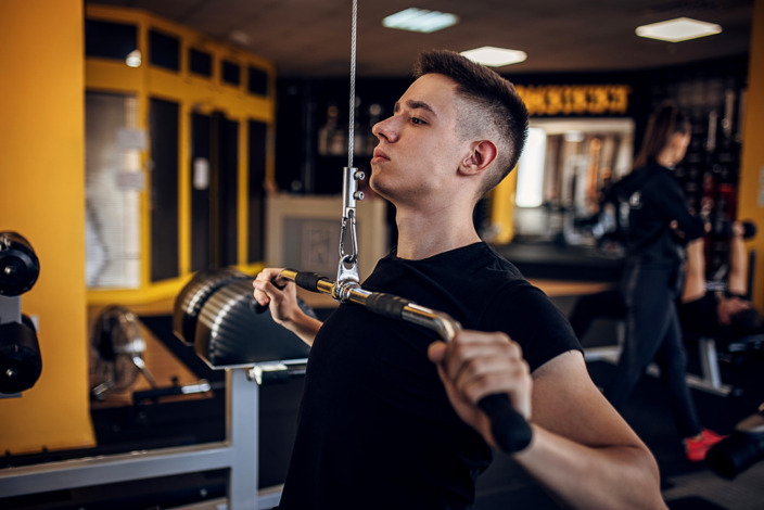 Mann steht im Fitnessstudio und trainiert seine Arme an einem Armzug.