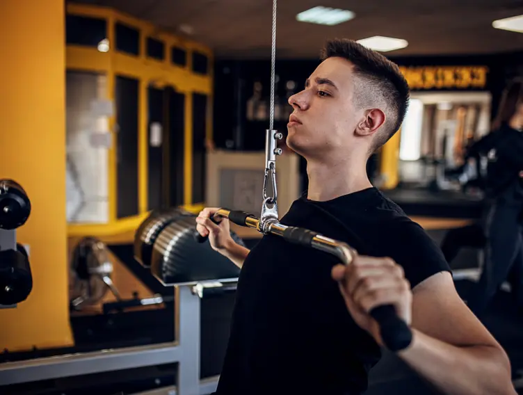 Mann steht im Fitnessstudio und trainiert seine Arme an einem Armzug.