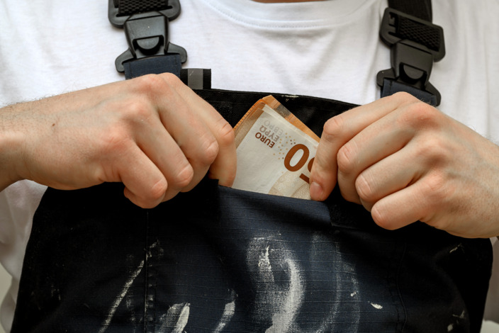 Handwerker steckt sich einen 50 Euro Schein in die Vordertasche der Latzhose