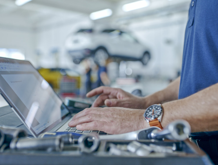 Mann steht in der Werkstatt und schaut auf seinen Laptop