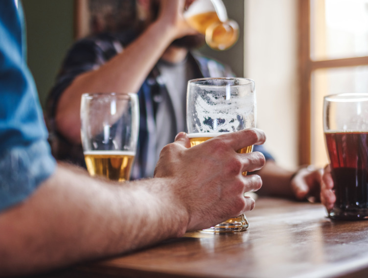 Männerhände die mit Bier gefüllte Gläser halten, während sie auf einem Tisch stehen
