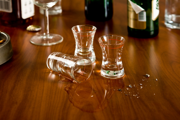 Ein Tisch mit leeren Schnapsgläsern, eins ist umgefallen und der Schnaps ausgekippt